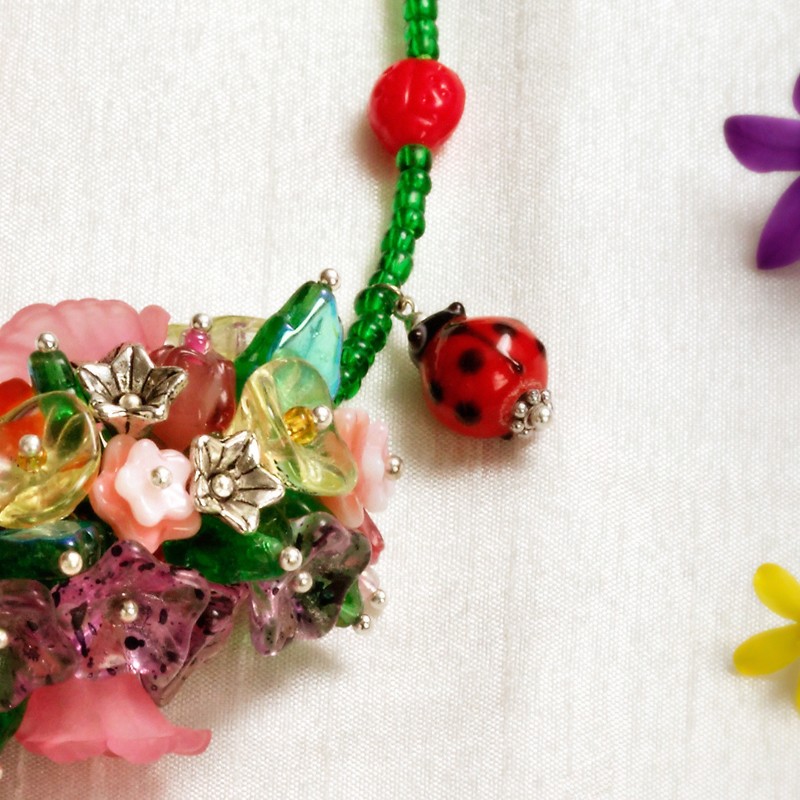 Schmuck-Set Mutschekiepchen, Nahaufnahme der Blütenperlen und des Käferanhängers im Zentrum der Kette Schmuck-Set Mutschekiepchen, Nahaufnahme der Blütenperlen und des Käferanhängers im Zentrum der Kette