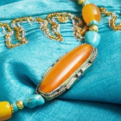 Halskette Nyima, Nahaufnahme der intarsienverzierten Focal-Perle aus bernsteinfarbenem Resin, flankiert von Türkis-Nuggets